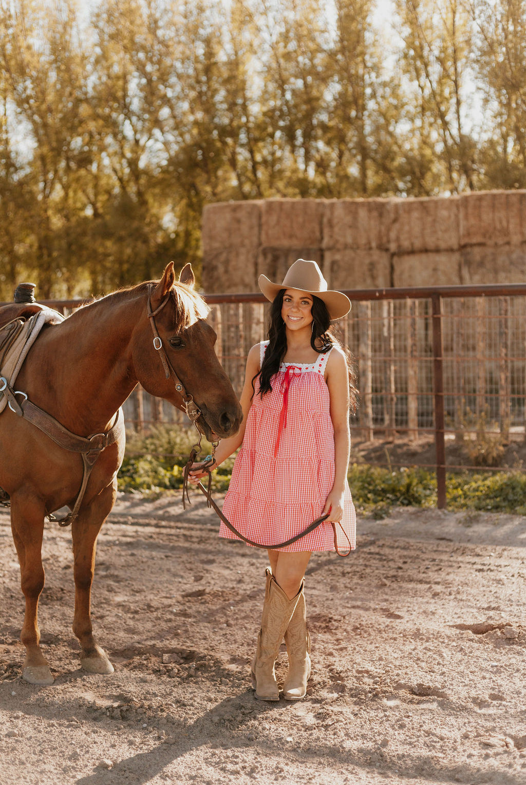 Woman wearing the Sweet Land of Liberty Gingham Dress while holding a horse saddle lace