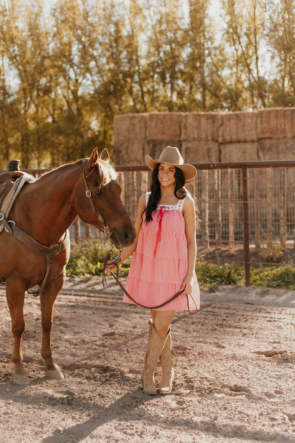 Woman wearing the Sweet Land of Liberty Gingham Dress while holding a horse saddle lace