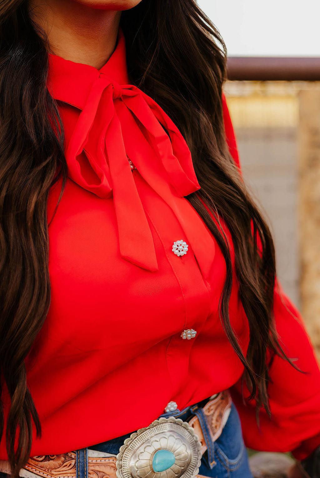 Close-up of red blouse with bow tie, turquoise belt buckle and long dark hair.