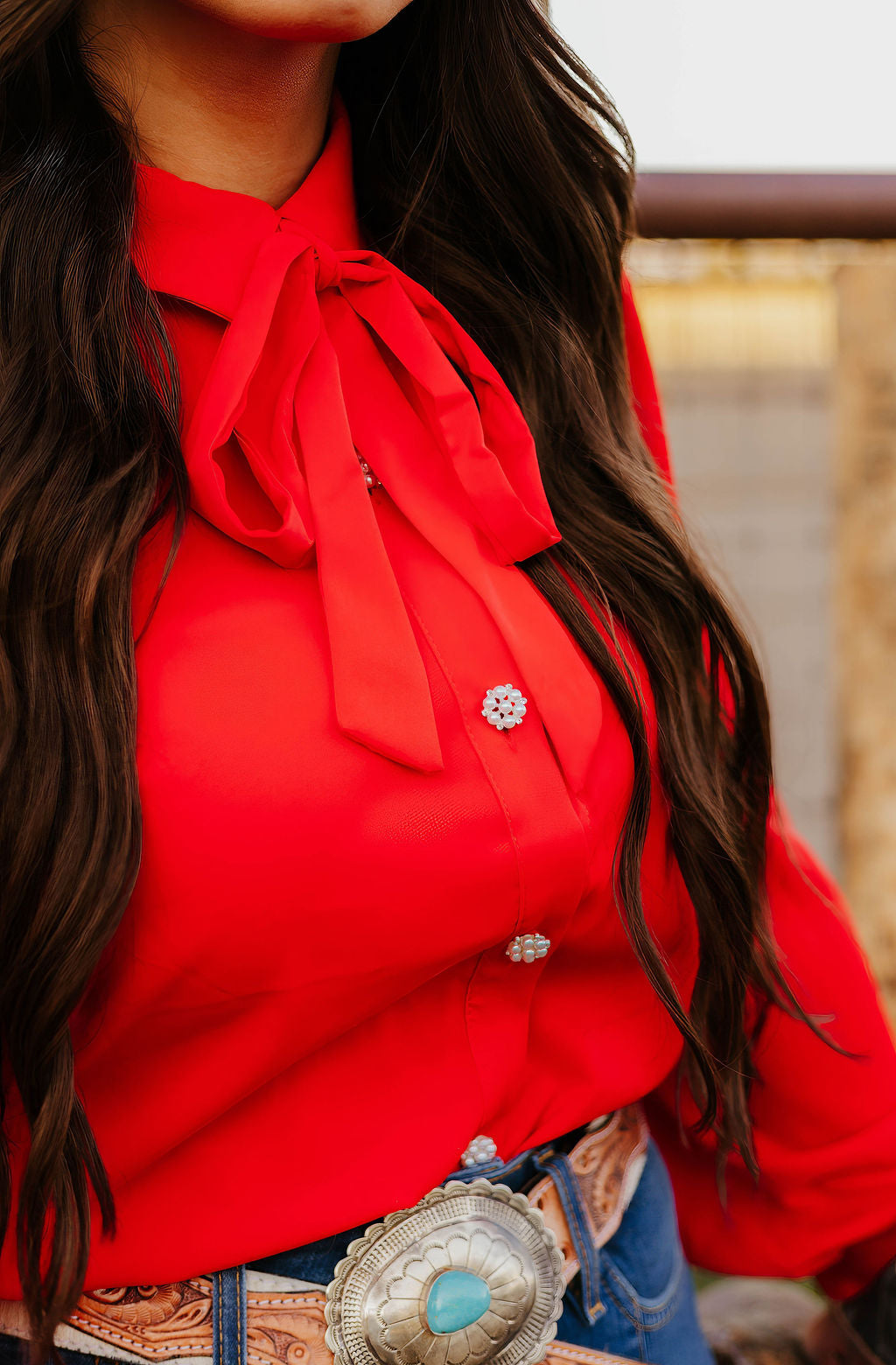 Close-up of red blouse with bow tie, turquoise belt buckle and long dark hair.
