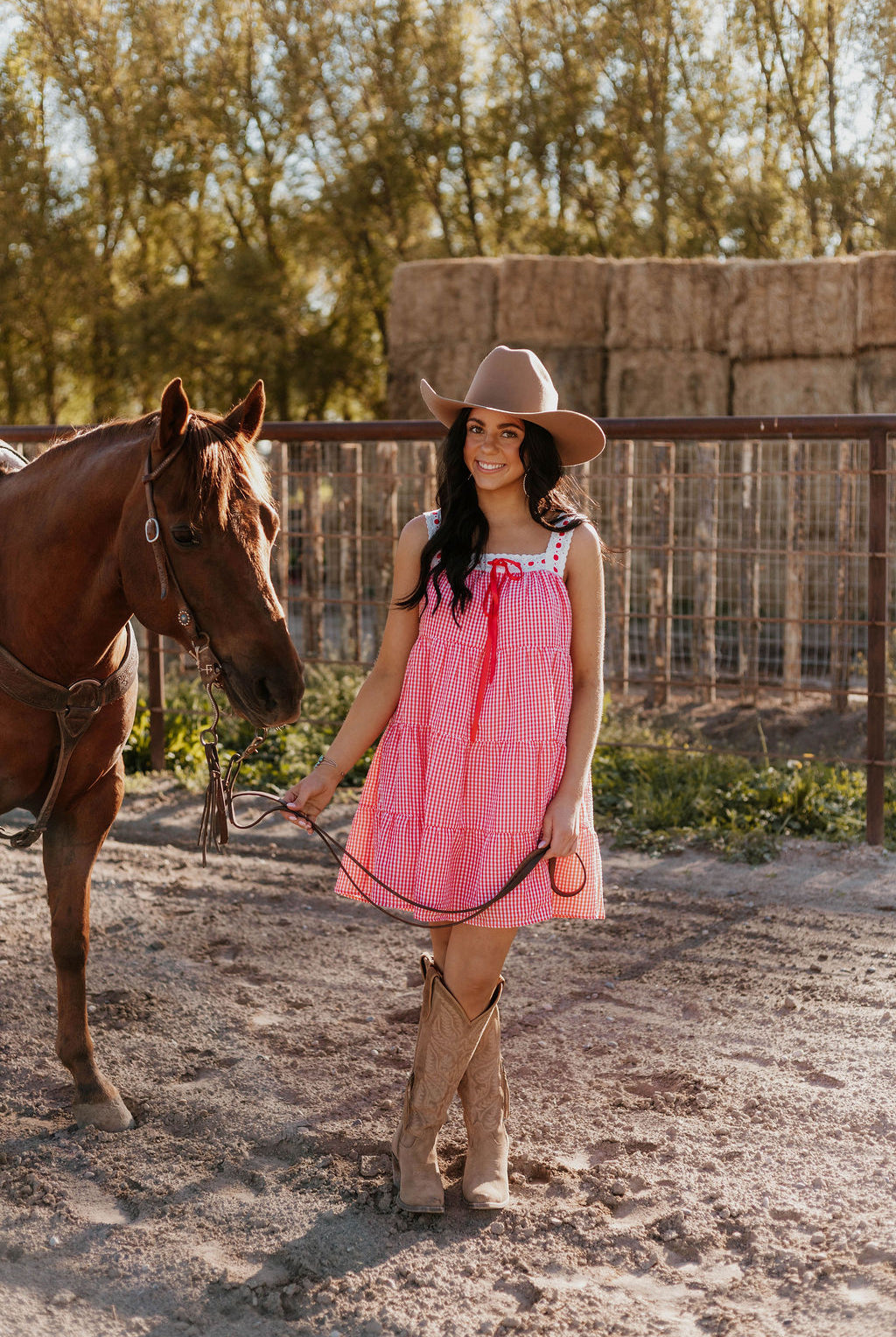 Woman wearing the Sweet Land of Liberty Gingham Dress while holding a horse saddle lace