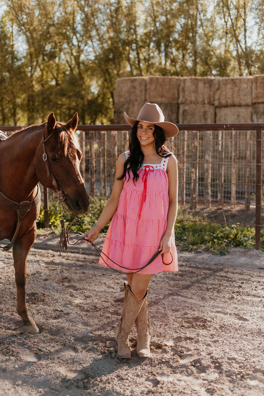 Woman wearing the Sweet Land of Liberty Gingham Dress while holding a horse saddle lace