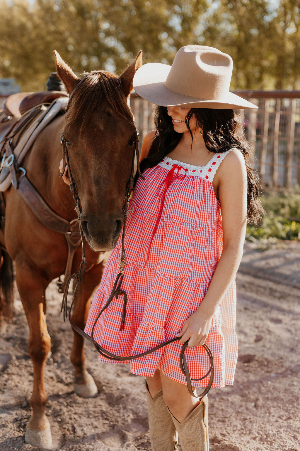 Close up of a horse and a woman wearing the Sweet Land of Liberty Gingham Dress while holding its saddle lace