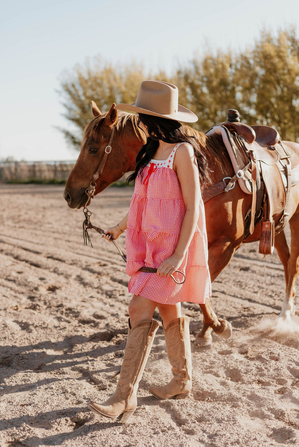 A woman wearing the Sweet Land of Liberty Gingham Dress leading a horse