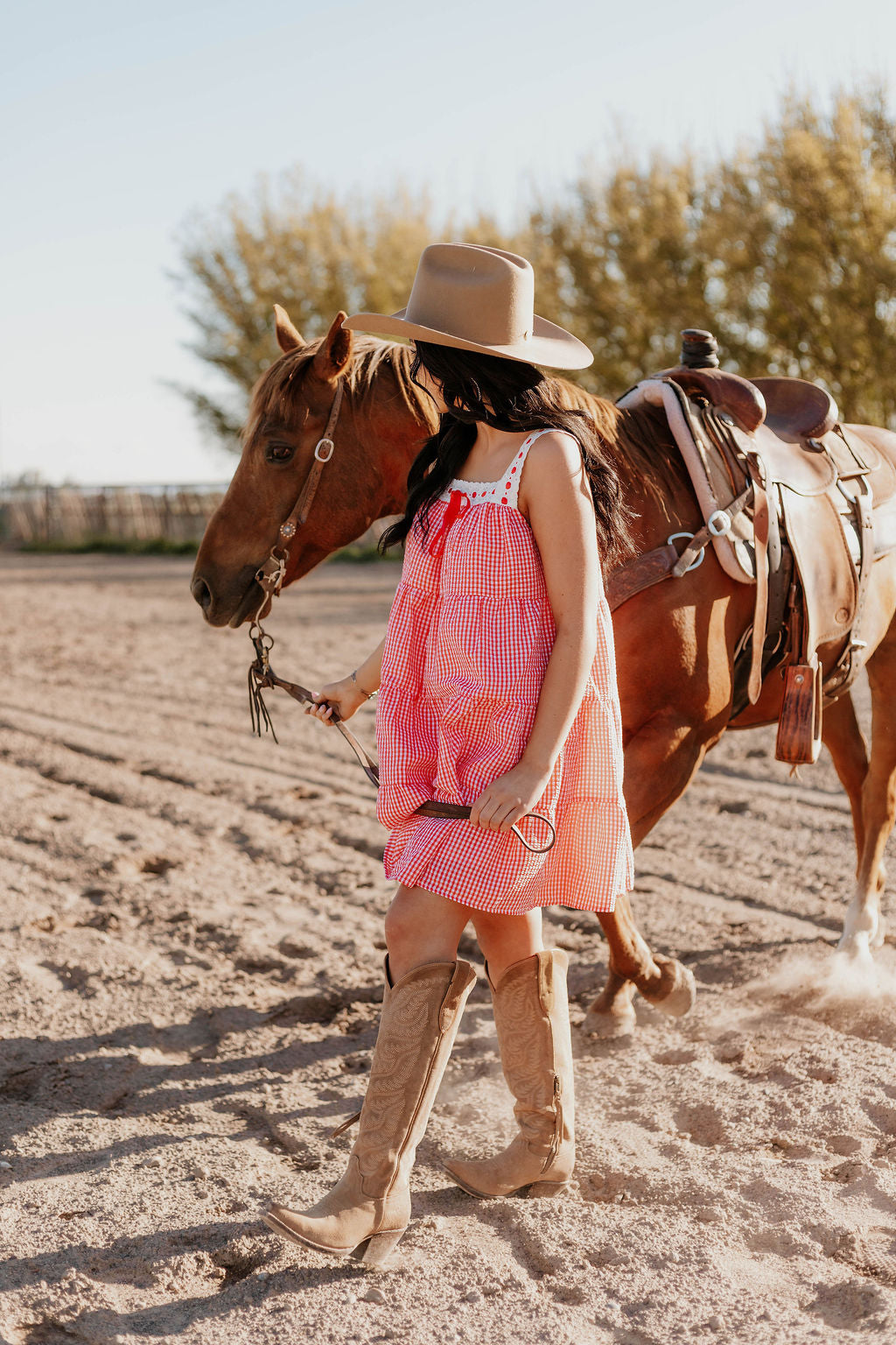 A woman wearing the Sweet Land of Liberty Gingham Dress leading a horse